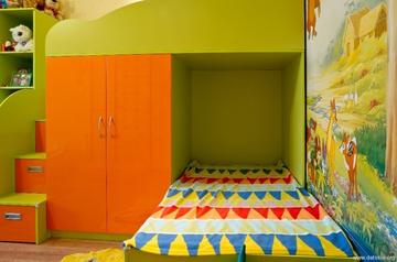 Детская двухъярусная кровать с перпендикулярным расположением спальных мест. Второй ярус кровати одной из сторон опирается на платяной шкаф для одежды и спальных принадлежностей.